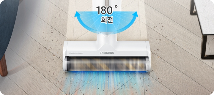 헤링본 마루가 깔린 거실 바닥을 배경으로 이미지 오른쪽 부분에는 화이트 상판의 테이블이 놓여 있고 이미지 왼쪽 부분에는 진한 남색 패브릭 소재의 소파 다리 부분이 노출되고 있습니다. 이미지 중간 부분에는 슬림 소프트마루 브러시로 청소를 하며 먼지를 흡입하는 모습의 이미지가 있고 슬림 소프트마루 브러시가 지나간 자리는 먼지가 있는 부분과는 달리 밝은 색으로 깨끗해진 모습을 알려주고 있습니다.
