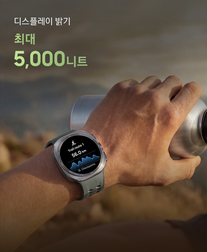 한 남성이 바위가 많은 산길을 걷고 있고, 물통을 든 손에는 올리브 색상의 마린 밴드를 장착한 티타늄 실버 색상의 갤럭시 워치 울트라2를 착용한 모습입니다. 화면에는 거리가 표시된 트레일 경로가 나타나 있어, 트레일 러닝이나 등반 시 까다로운 야외 환경에서도 신뢰할 수 있는 길 안내를 제공하는 점을 표현합니다.