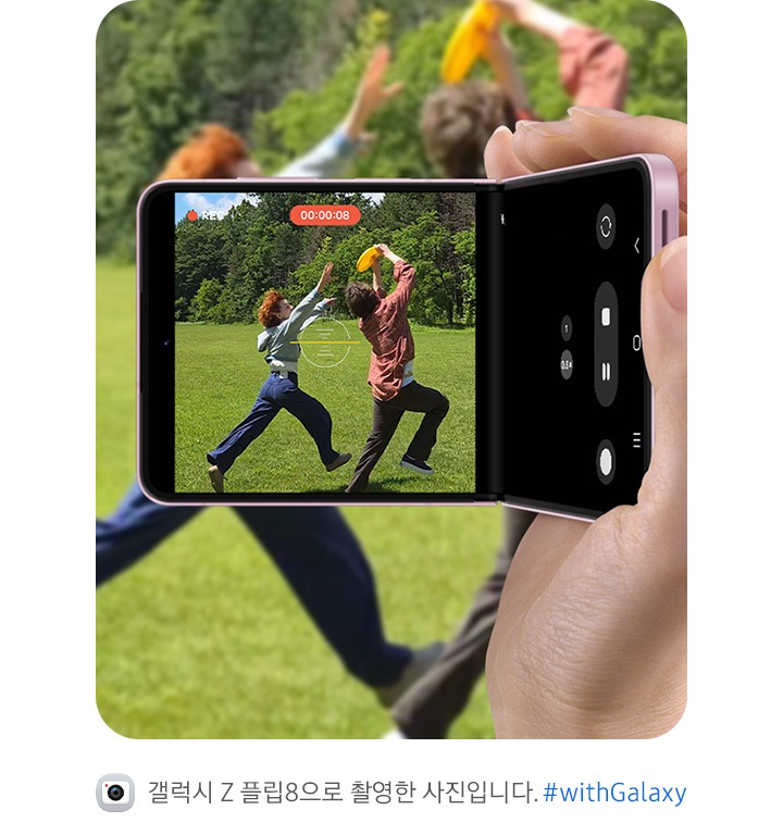 갤럭시 Z 플립8을 캠코더처럼 손에 들고 야외에서 즐겁게 놀고 있는 두 친구를 촬영하는 모습입니다. 수평 고정 슈퍼 스테디의 수평 잠금 기능 덕분에 영상이 흔들림 없이 안정적으로 유지되는 것을 강조하고 있습니다. 