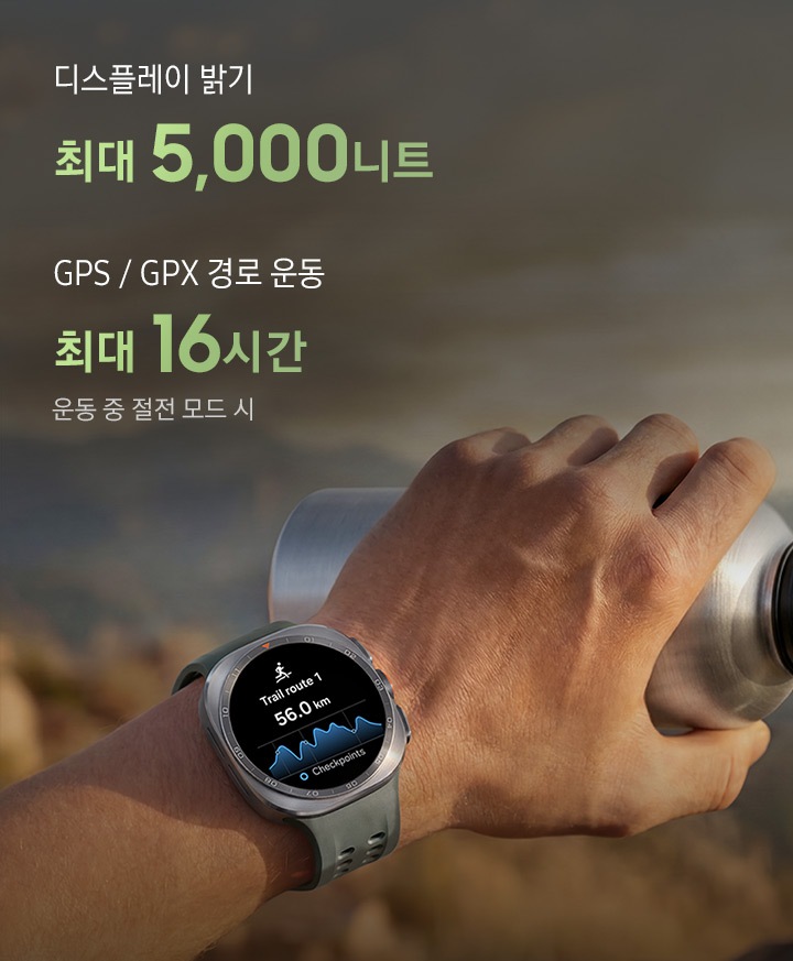 한 남성이 바위가 많은 산길을 걷고 있고, 물통을 든 손에는 올리브 색상의 마린 밴드를 장착한 티타늄 실버 색상의 갤럭시 워치 울트라2를 착용한 모습입니다. 화면에는 거리가 표시된 트레일 경로가 나타나 있어, 트레일 러닝이나 등반 시 까다로운 야외 환경에서도 신뢰할 수 있는 길 안내를 제공하는 점을 표현합니다. 이미지 내에는 '디스플레이 밝기 최대 5,000니트, GPS / GPX 경로 운동 최대 16시간 운동 중 절전 모드 시' 문구가 있습니다.