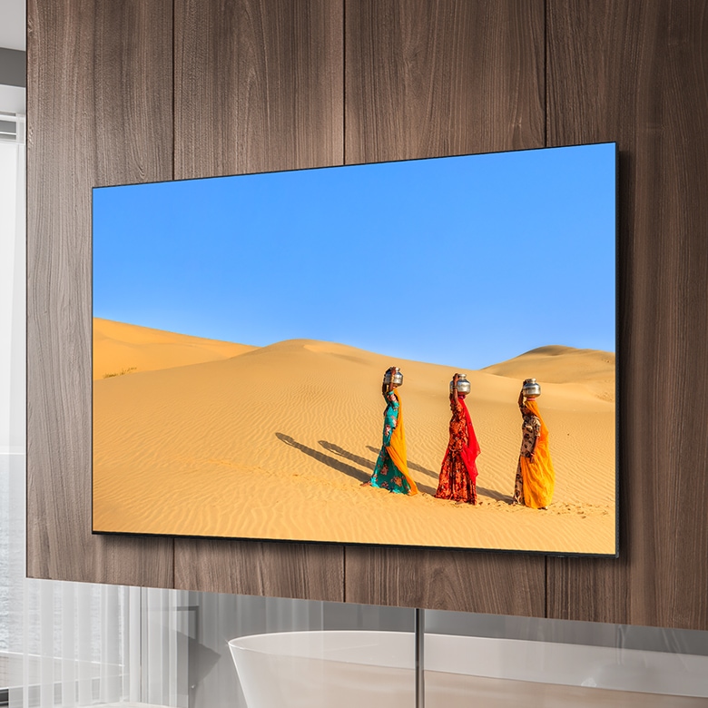 벽걸이형 삼성 TV 화면에 머리에 항아리를 얹고 사막을 걷는 3명의 여성이 표시되어 있습니다.