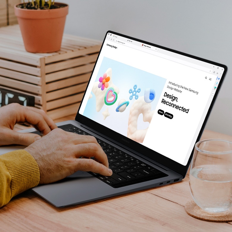 삼성 갤럭시 북 제품이 놓여있고 타이핑치는 남자 손이 보입니다. 