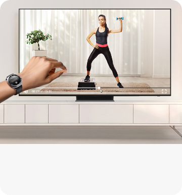 왼편에 갤럭시 워치를 착용한 손목이 보이며 중앙 뒷편의 TV 화면에는 홈트레이닝 영상이 나오고 있다