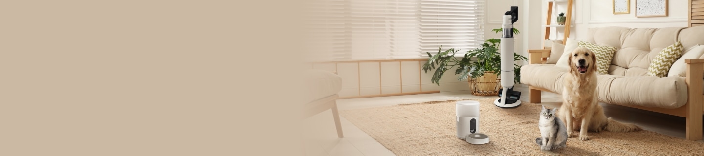 정면을 바라보는 대형견 1마리, 회색 고양이 한 마리, 바닥에 세워져 있는 스탠드형 청소기와 반려동물 자동급식기, 쿠션이 놓인 소파