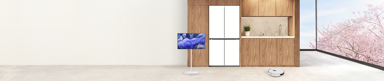 우측 통창 밖으로 벚꽃이 만개한 풍경 이미지와 중앙 우드톤의 벽에는 키친핏 냉장고와 그 좌측으로 무빙스타일, 우측 바닥에 로봇 청소기가 배치된 라이프 스타일 컷