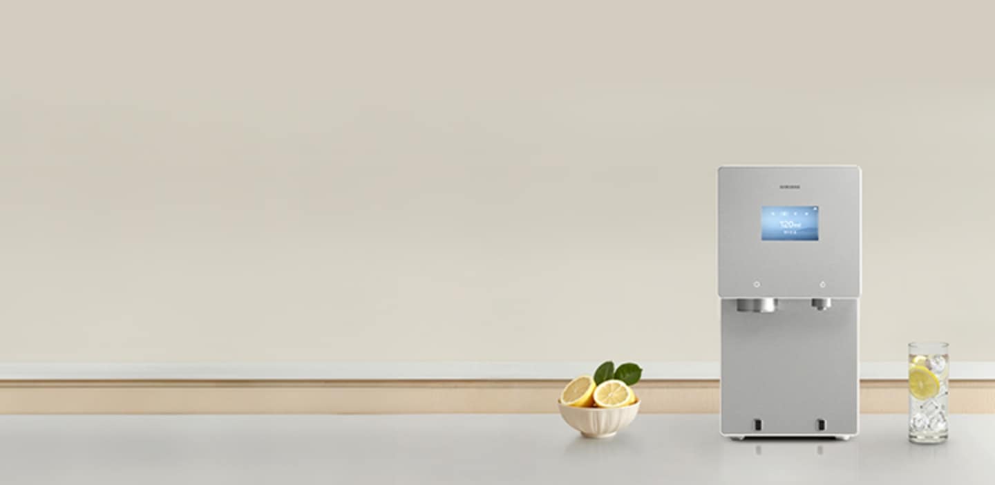 회색톤의 대리석 주방 상판 위에 2026 Bespoke AI 얼음정수기 신제품이 놓여져 있고 제품 좌측에 레몬이 담긴 그릇, 우측에는 레몬과 얼음물이 담긴 컵이 놓여있는 이미지 
