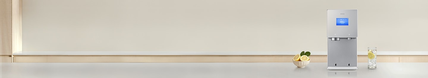 회색톤의 대리석 주방 상판 위에 2026 Bespoke AI 얼음정수기 신제품이 놓여져 있고 제품 좌측에 레몬이 담긴 그릇, 우측에는 레몬과 얼음물이 담긴 컵이 놓여있는 이미지 