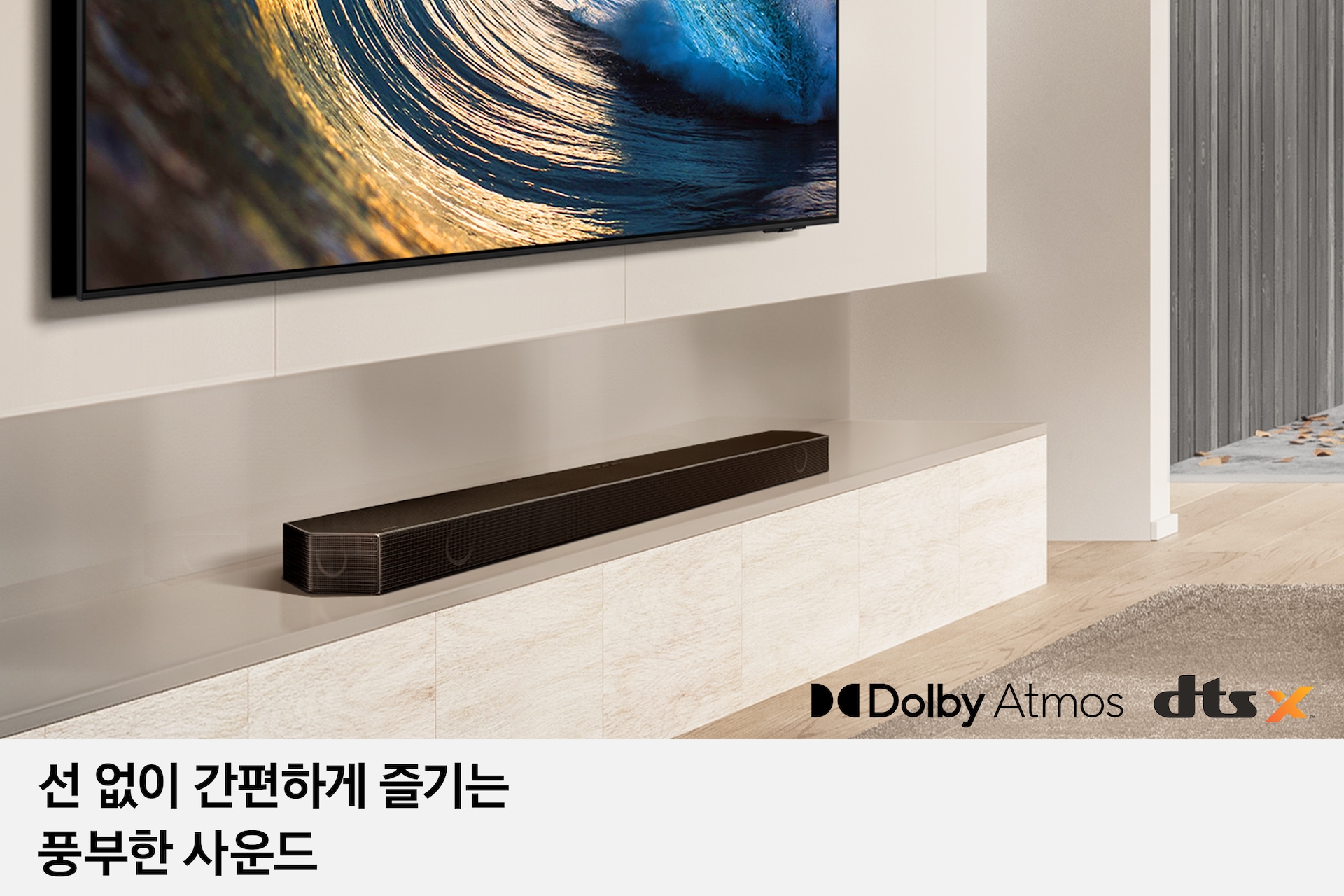 [벽면에는 TV가 설치되어 있습니다. 그 아래 장식장에 사운드바가 놓여 있습니다. 오른쪽 하단에는 Dó~lbý Á~tmós~와 dtsX~ 로고가 있습니다. 선 없이 간편하게 즐기는 풍부한 사운드 féát~úré 컷입니다.] 