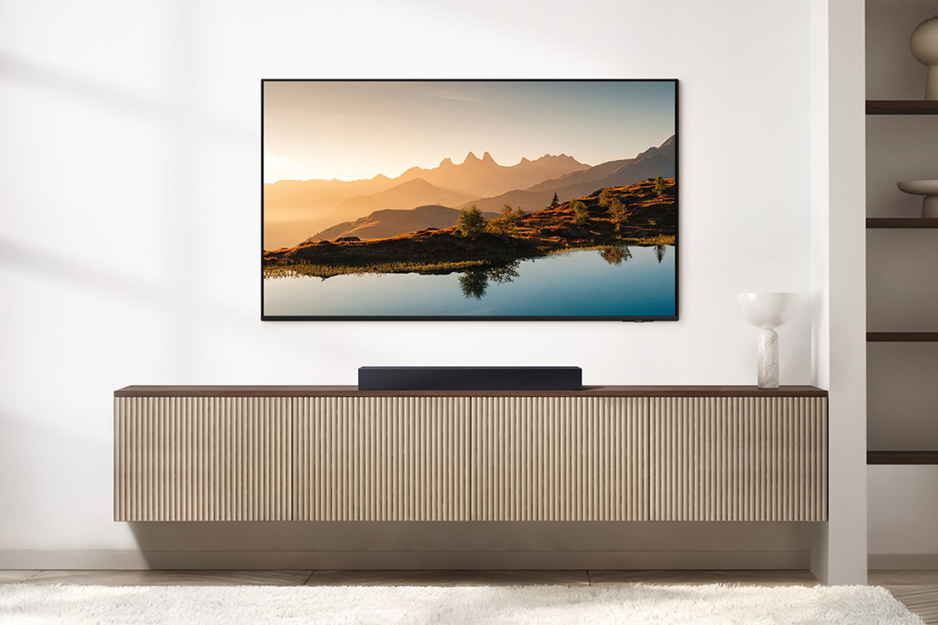 벽에 TV가 설치되어 있으며, TV 하단에는 장식장이 놓여 있습니다. 그 위에 사운드바가 놓여 있는 라이프스타일 컷입니다.