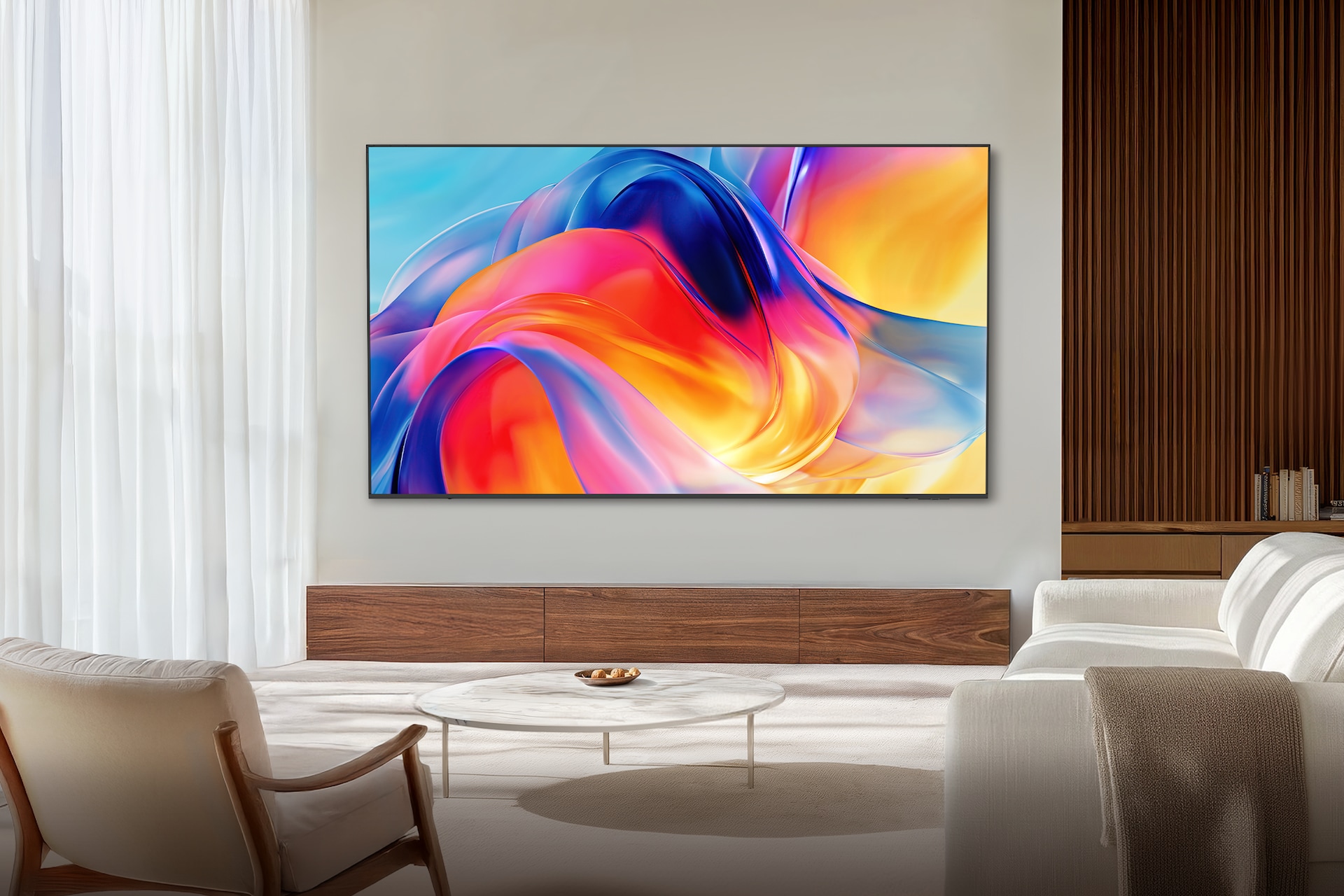 거실 벽에 TV가 설치되어 있습니다. TV 아래에는 장식장이 놓여 있으며, TV 앞에는 테이블과 1인용 의자, 소파가 놓여 있습니다.