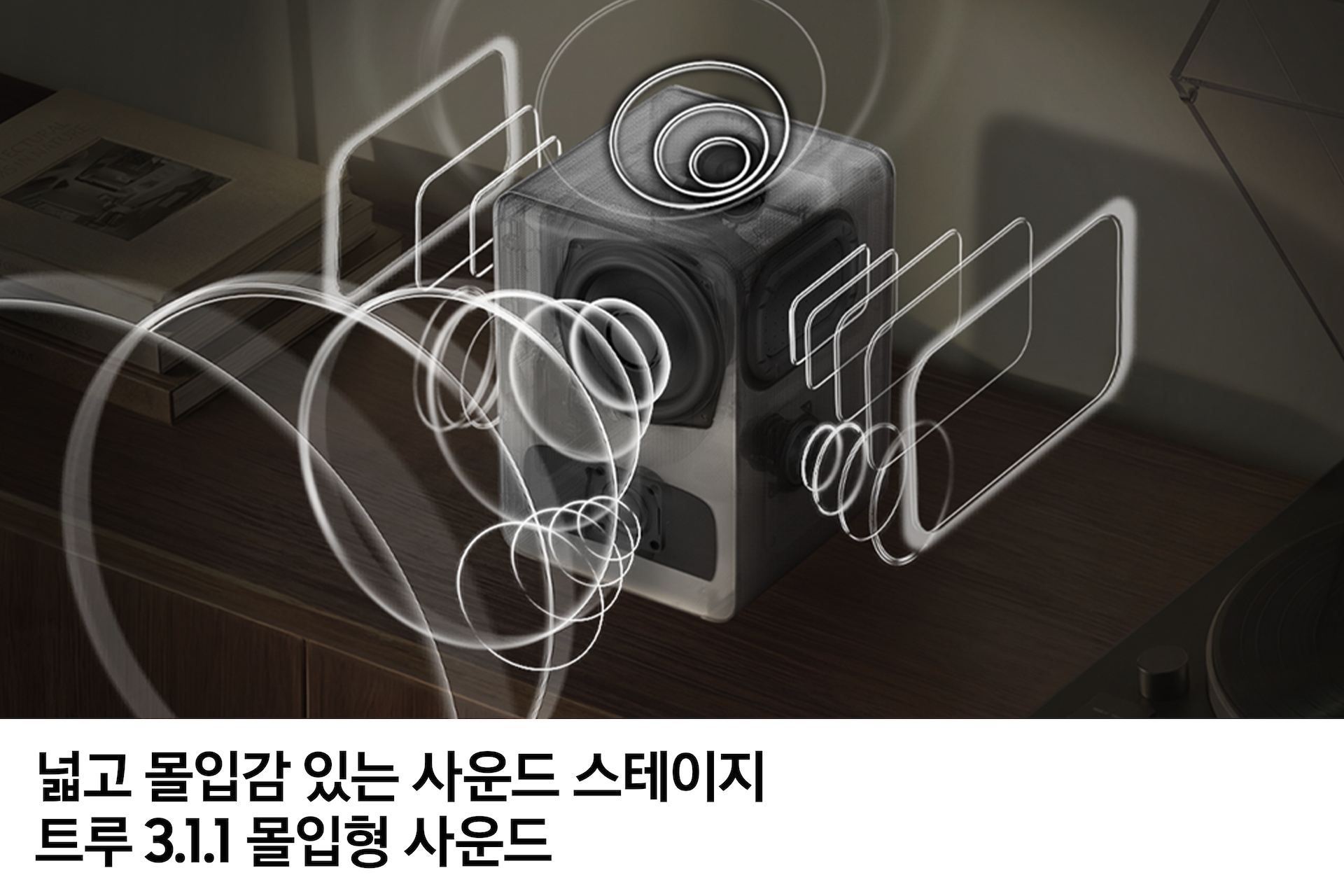 장식장 위에 놓인 스피커에서 음향효과가 나오고 있습니다. 이미지 하단에는 '넓고 몰입감 있는 사운드 스테이지 트루 3.1.1 몰입형 사운드' 문구가 기재되어 있습니다.