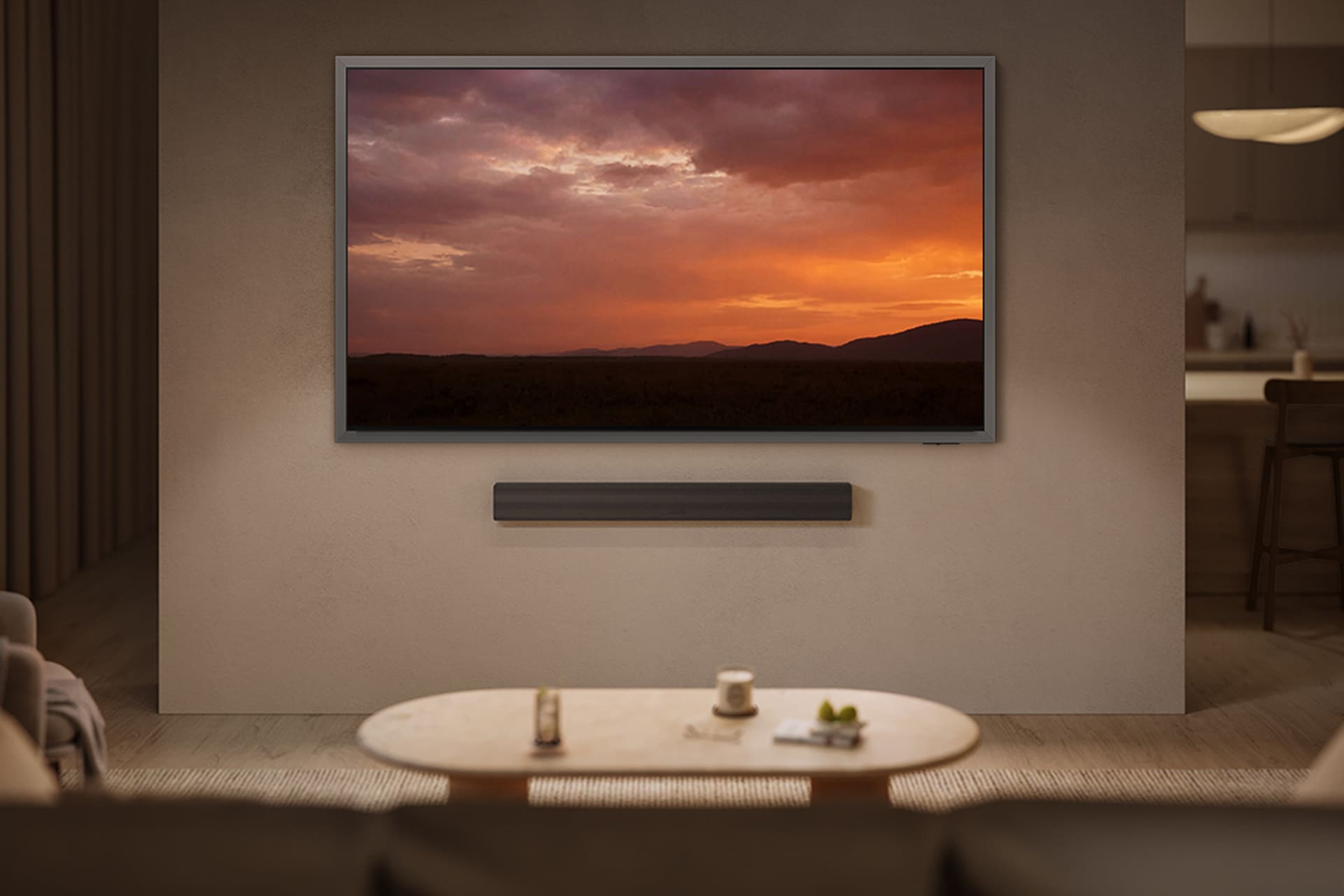 거실 벽에 TV와 사운드바가 설치되어 있습니다. 화면에는 산과 노을이 보입니다. TV 앞에는 향초와 컵이 놓여진 테이블과 소파가 있습니다.