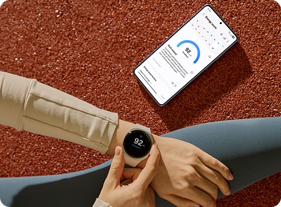 한 사람이 실버 색상의 갤럭시 워치8을 착용하고 있습니다. 화면에 에너지 점수 92점이 표시됩니다. 그 다음에 갤럭시 S26 울트라에 최신 에너지 점수가 표시됩니다.