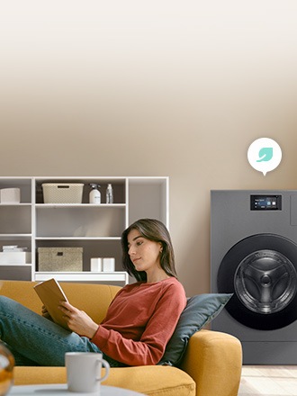소파에 앉아 책을 읽는 여성 옆에서 블랙 색상의 삼성 Bespoke 올인원 콤보가 세탁을 진행하고 있으며 세탁기 위에 나뭇잎 아이콘이 표시됨