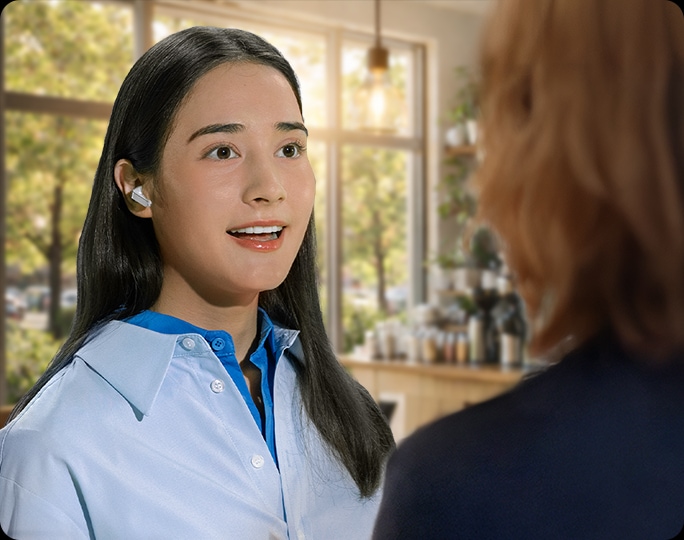 한 여성이 화이트 색상의 갤럭시 버즈4 프로 이어버드를 착용한 상태로 다른 사람과 대화를 나누며 대화 감지 기능을 표현하고 있습니다.