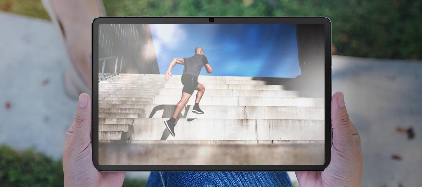 야외에서 갤럭시 탭 S10 FE+를 들고 있는 모습으로 화면에 눈부심과 반사가 보이고 있습니다.