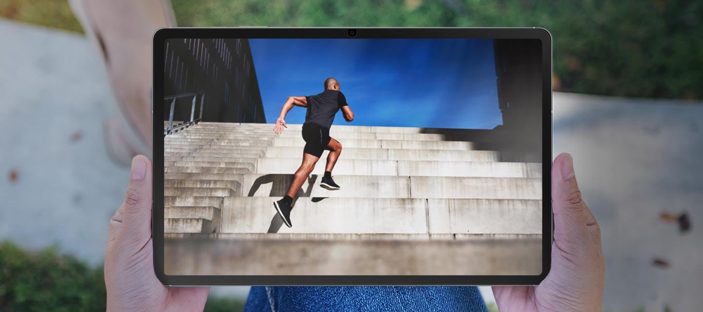 AR 스크린 프로텍터을 부착한 갤럭시 탭 S10 FE+를 야외에서 사람이 들고 있는 모습으로 화면의 눈부심과 반사가 감소되어 있습니다.