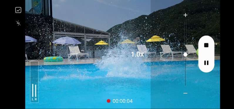 La interfaz de la aplicación de la cámara para el control del zoom se ve en la parte superior del video. El zoom de la cámara se acerca 3x hasta un hombre en un trampolín listo para saltar. Cuando salta, la cámara se aleja rápidamente hasta 1x para captar la zambullida. 