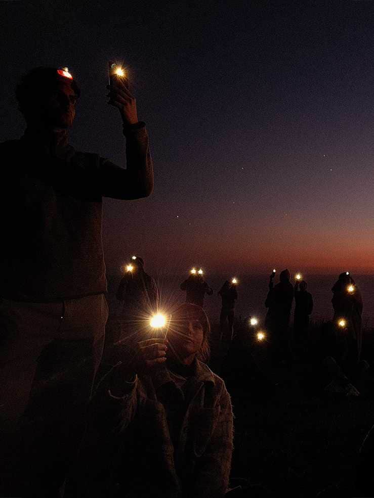 Foto tomada en Galaxy S20 Ultra con Modo Profesional a un grupo de personas que usan faros y la linterna de sus teléfonos para crear una constelación en el cielo nocturno