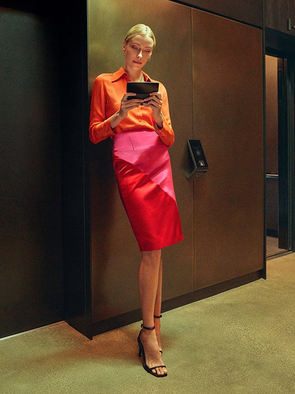 Una mujer parada junto a un ascensor, que sostiene un Galaxy Z Fold4 desplegado y mirando su pantalla principal con atención.