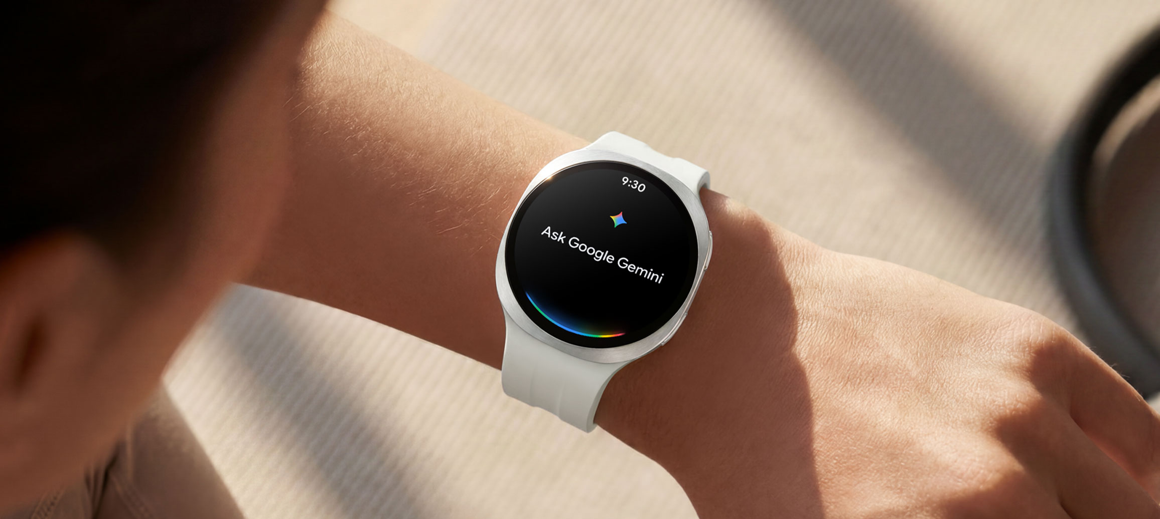 A person wearing Galaxy Watch9 in Cream with a Sport Band in Cream raises their wrist to give a voice command to their watch using Google Gemini. Google Gemini icon and text Ask Google Gemini shown on the watch display.