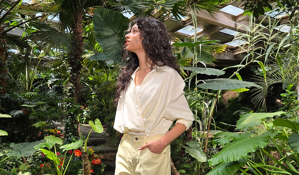 Une femme debout avec des plantes autour d’elle. Avec Super HDR, des réglages de luminosité appropriés sont appliqués à la photo.