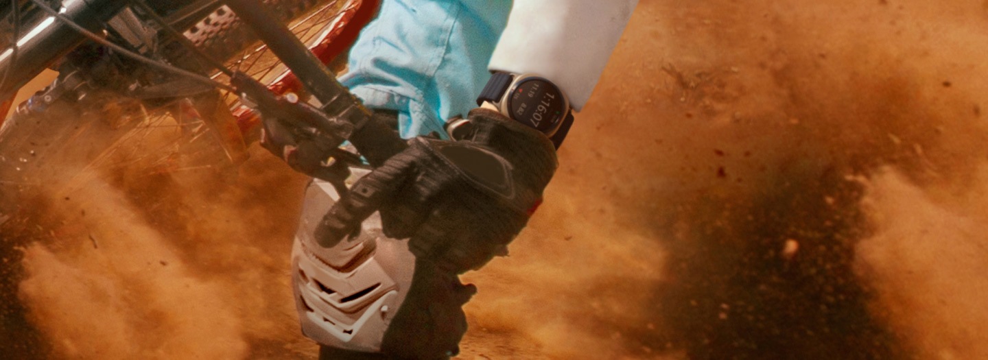 Primer plano de una persona pedaleando en el desierto con las manos enguantadas en el asa. El Galaxy Watch Ultra está en la muñeca.