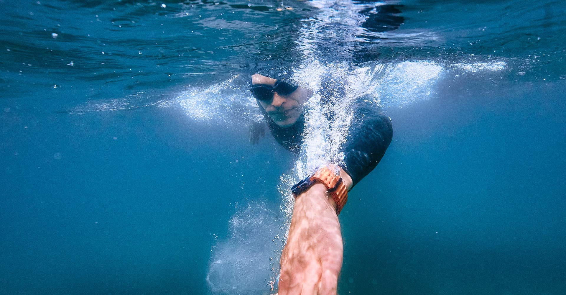 A man in a swimsuit is swimming in the ocean, making a stroke into the water with a Galaxy Watch Ultra on his wrist.