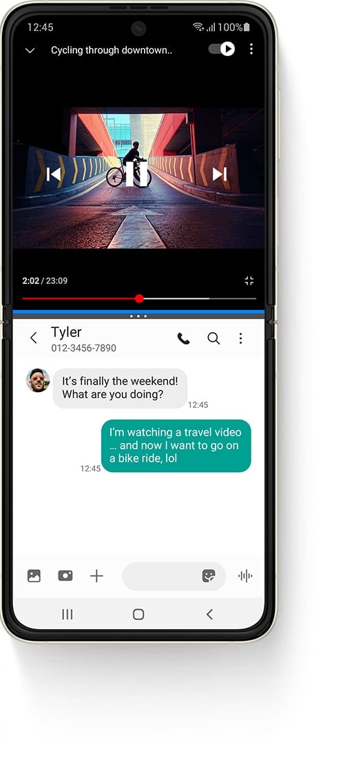 Galaxy Z Flip3 5G unfolded in Multi Active Window, with a YouTube video on top, a video called Cycling Through Downtown and a person standing on a bike on a ramp. The Messages app on the bottom and the received text message from Tyler says "It's finally the weekend! What are you doing?" The sent text message says "I'm watching a travel video... and now I want to go on a bike ride, lol"