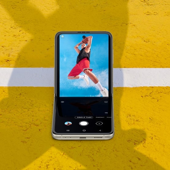 A man holding a basketball over his head and jumping while looking into the camera. Galaxy Z Flip3 5G seen in Flex mode with the Camera app on the Main Screen, and the same photo seen in the viewfinder.