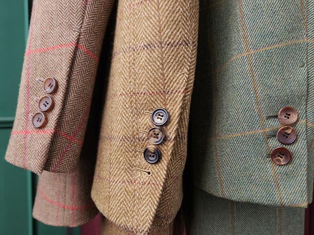 Three jackets in different colors with windowpane check patterns hang next to each other. The high resolution of the photo allows the texture of the fabric to be seen clearly.