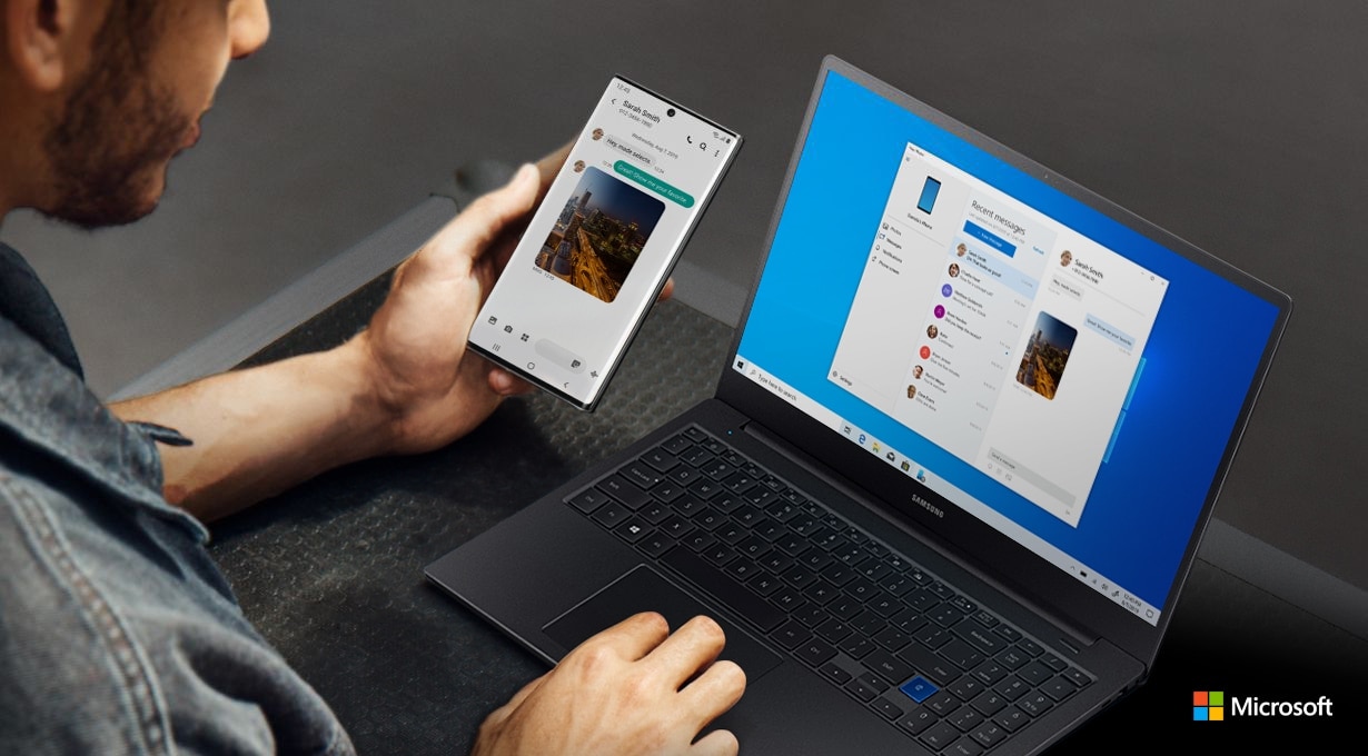 Man working on a laptop and holding Galaxy Note10 plus. Both the laptop and the phone have the same text message conversation onscreen, showing how Link to Windows syncs messages to your PC