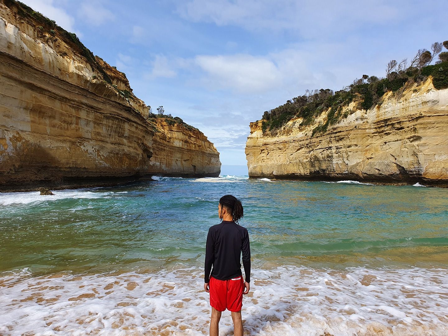 Photo captured by Galaxy S10 plusâs Wide-angle Camera of a man standing in a body of water in front of seaside cliffs.