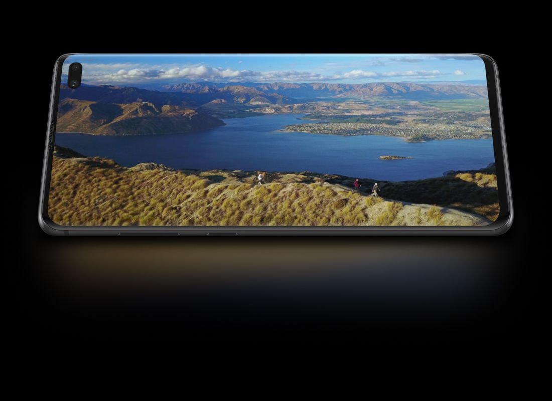 Galaxy S10 plus in landscape mode seen from the front with a photo of people hiking along seaside cliffs shown onscreen. While scrolling, the phone starts to tilt back.