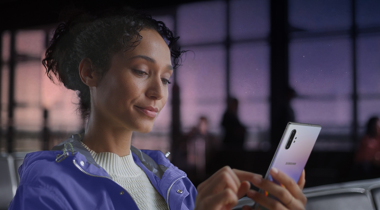 Woman holding Galaxy Note10+. Download manager notifications appear showing two large files being downloaded at the same time thanks to the improved data speeds