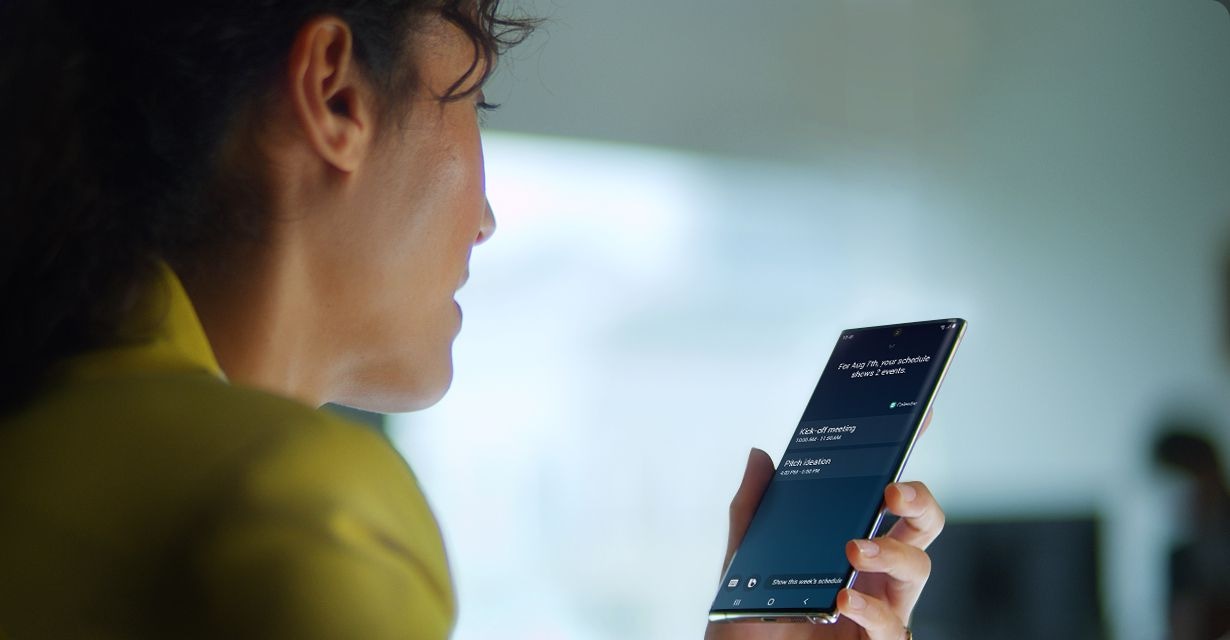 Woman holding Galaxy Note10+ with the Bixby GUI onscreen displaying tomorrow’s schedule. Three Bixby notifications appear saying “How’s the weather tomorrow?”, “Text Alice See you at 10”, and “Read tomorrow’s schedule.”