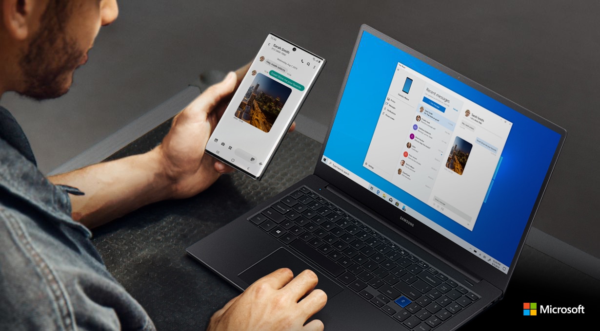 Man working on a laptop and holding Galaxy Note10+. Both the laptop and the phone have the same text message conversation onscreen, showing how Link to Windows syncs messages to your PC