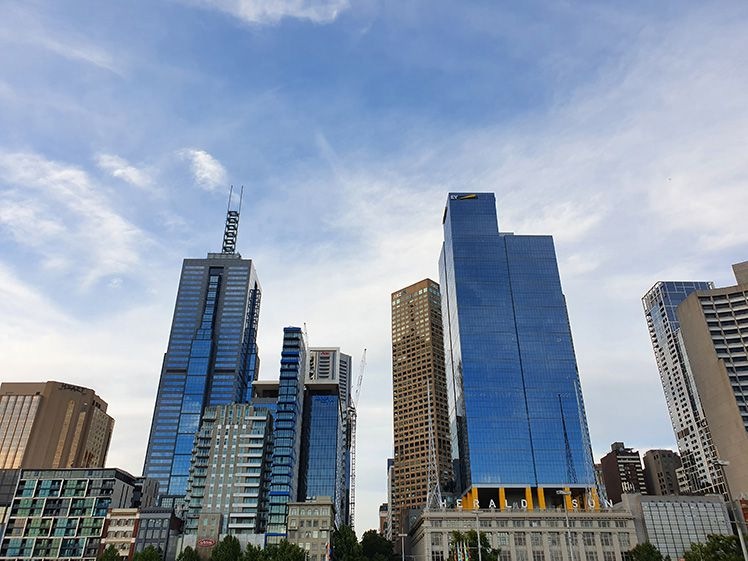 Fotografia zachytená na Galaxy S10 + zobrazujúca pohľad na výškové budovy v jasnom dennom svetle na pozadàs modrou oblohou a oblohou odrážajúcou sa v niektorých budovách.
