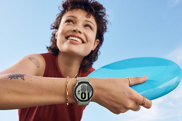 ผู้หญิงคนหนึ่งยิ้มและถือจานร่อนอยู่พร้อมกับสวม Galaxy Watch4 อยู่ตรงข้อมือ