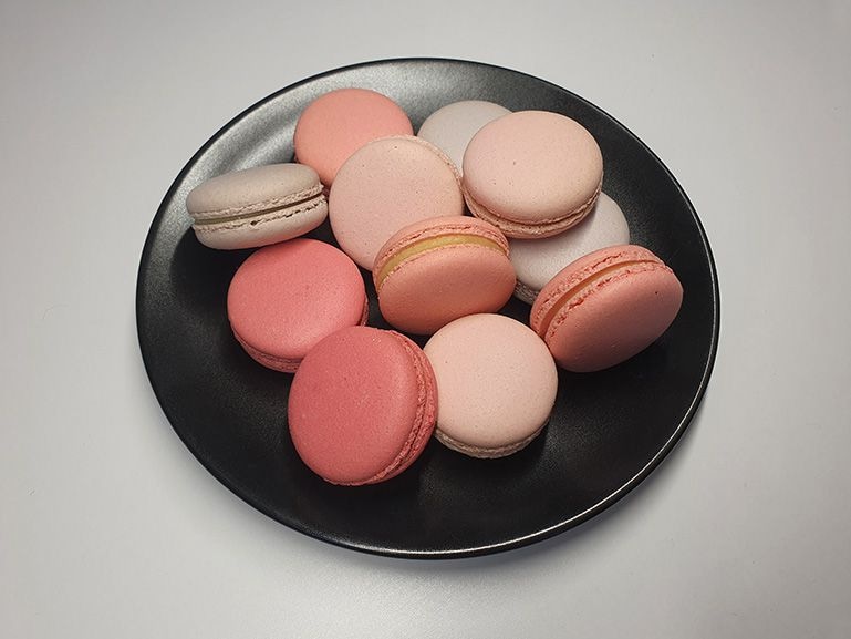 Photo captured by Galaxy S10 plus of a plate with pastel macarons piled on top. An animated swipe shows how Scene Optimizer enhances the color and tone.