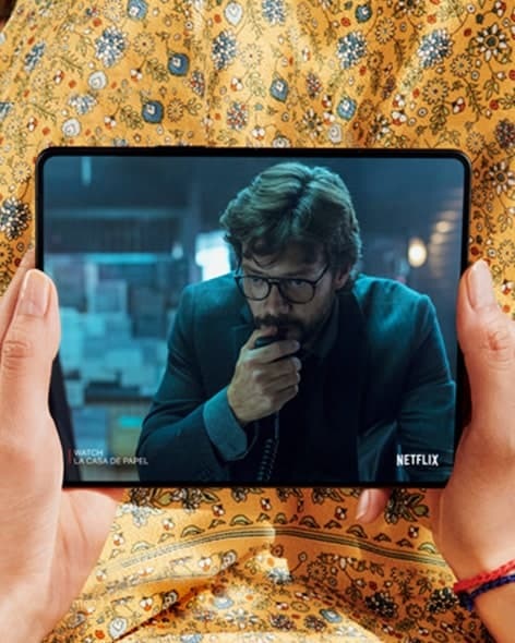Eller açık bir Galaxy Z Fold3 5G'yi tutmaktadır. Ana Ekran, elini yüzünde tutan bir adamın görüldüğü bir Netflix videosu sahnesini sergiler.