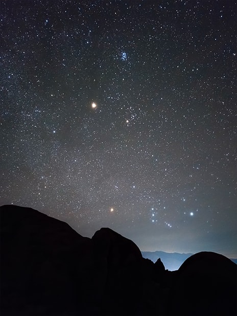 A night landscape photo with the silhouette of mountainous terrain in the foreground. Details of the starry sky are clearly captured in high-resolution detail with Expert Raw.