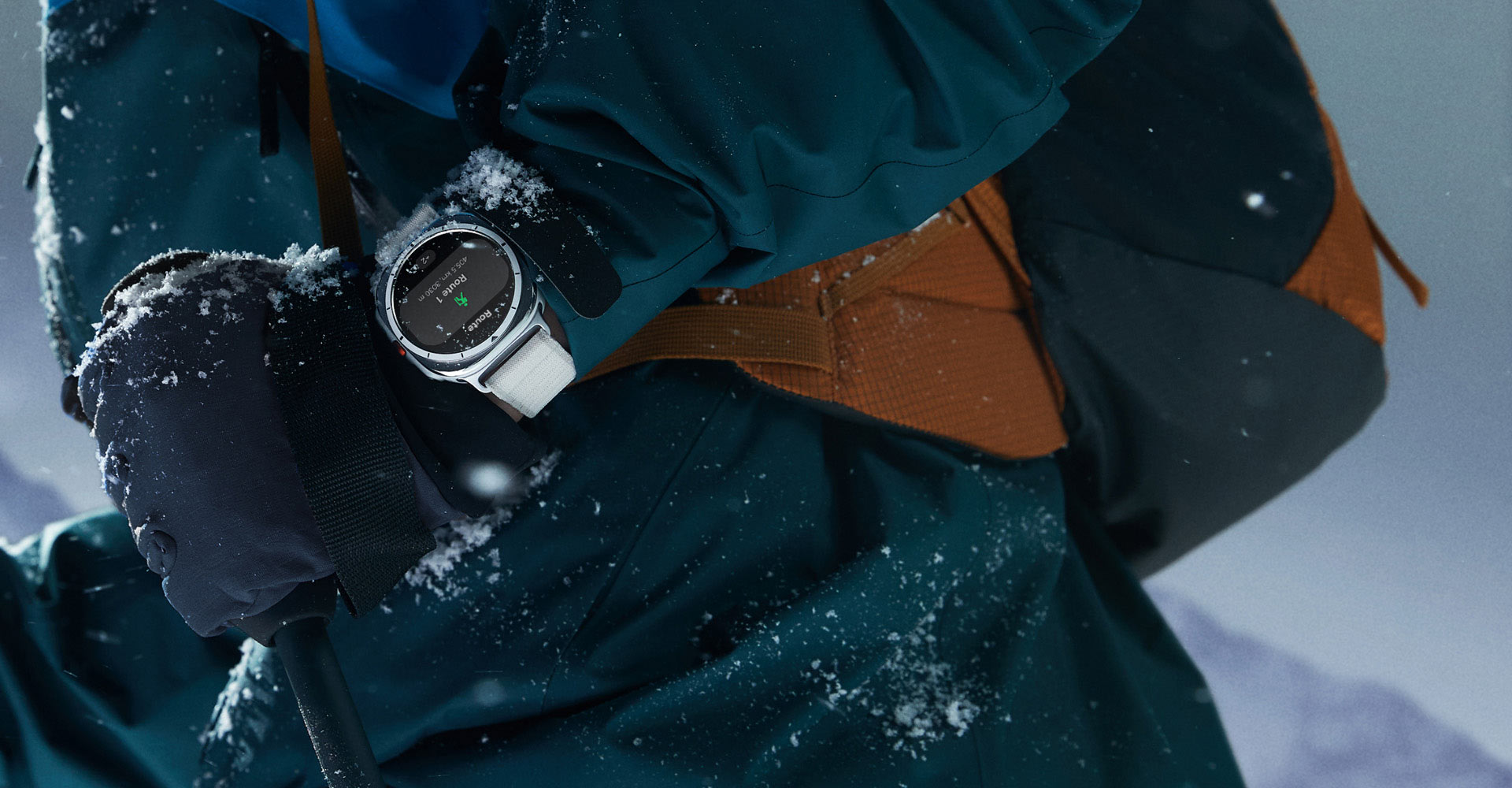 A person wearing mountain climbing gear, with a bit of snow on them, has a Galaxy Watch Ultra on their wrist.