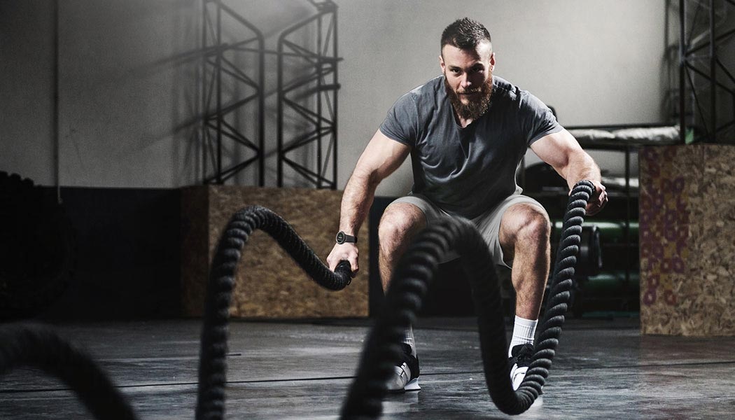 Various exercise symbols are shown as an icon and a workout icon is highlighted. A man is energetically using exercise ropes while wearing a Galaxy Watch4 Classic device.