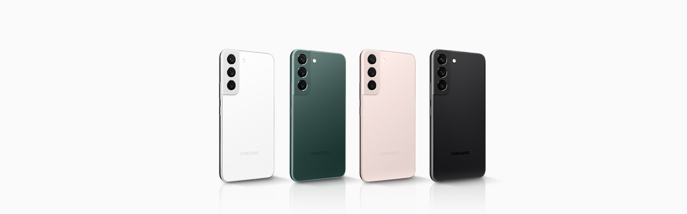 Four Galaxy S22&#39;s stand in one row with their rear sides facing forward, as they all face right at an angle. From left to right, the colors go: Phantom White, Green, Pink Gold and Phantom Black. 