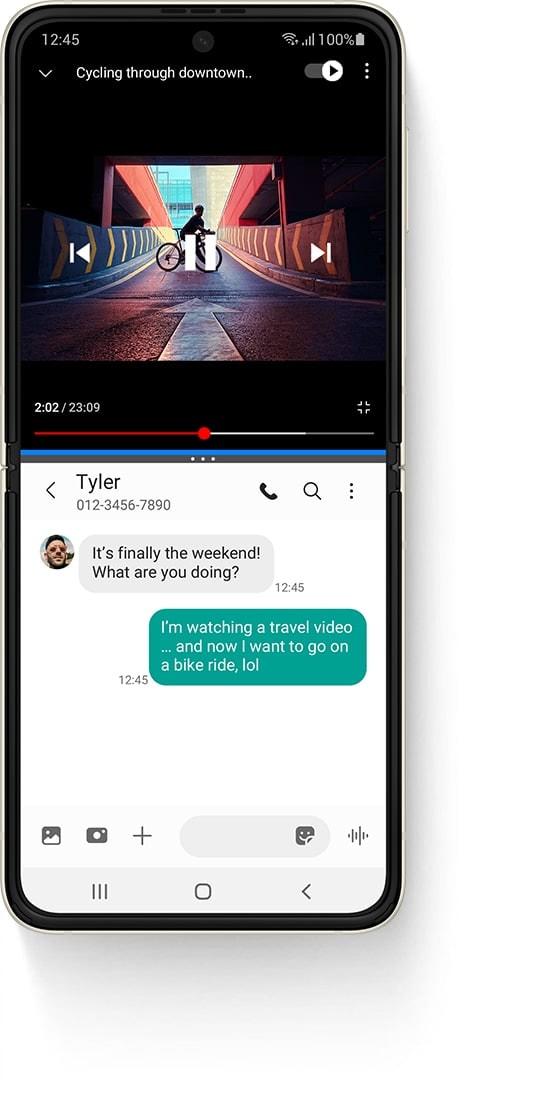 Galaxy Z Flip3 5G unfolded in Multi Active Window, with a YouTube video on top, a video called Cycling Through Downtown and a person standing on a bike on a ramp. The Messages app on the bottom and the received text message from Tyler says it's finally the weekend! What are you doing?. The sent text message says I'm watching a travel video... and now I want to go on a bike ride, lol.
