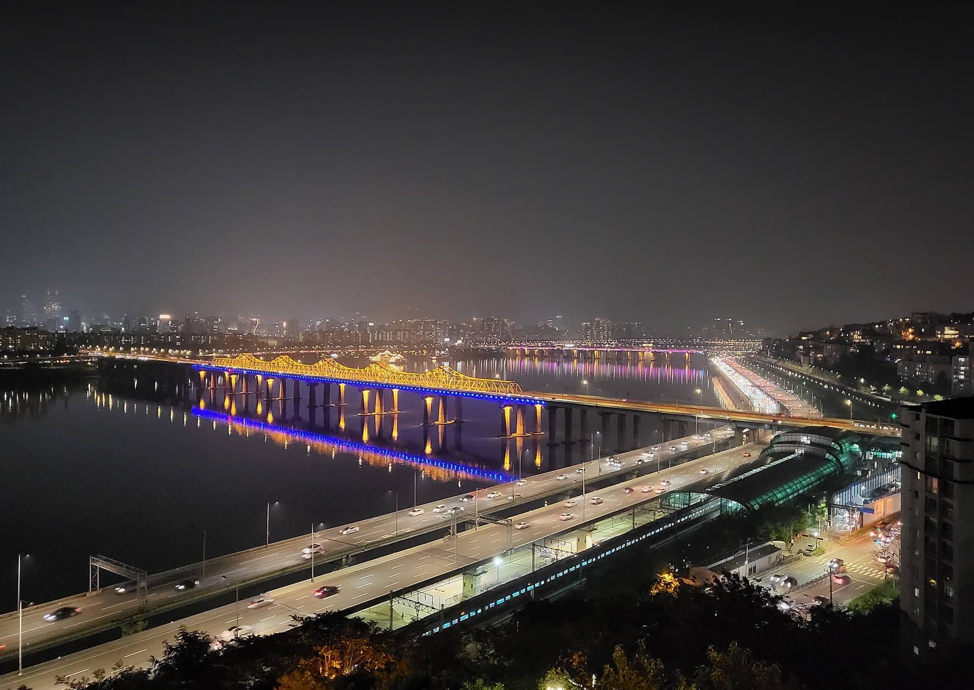 A view of a cityscape at night, as seen from the top of a hill. Galaxy Z Flip3 5G in Flex mode with the Camera app on the Main Screen and the same cityscape in the viewfinder, being recorded with Night Hyperlapse.