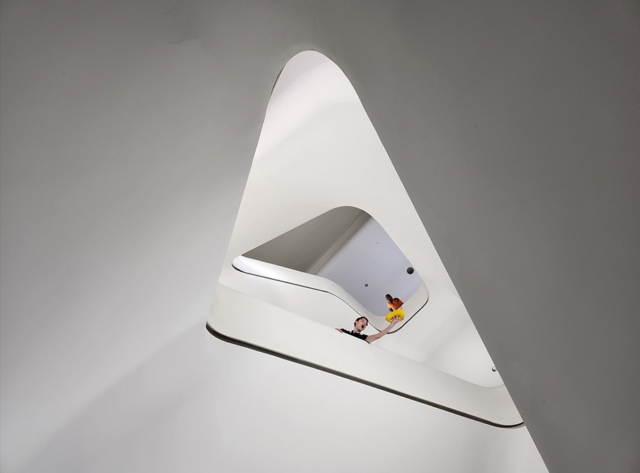 A view looking up a circular staircase of a large, modern building. Many floors up, a man is seen leaning over the handrails. Another man is seen with his arm extended over the railing, catching a yellow hat that seems to have fallen from above. Next is a close up of the man at the top of the staircase. With 30 X Space Zoom, the photo captures his shocked expression in reaction to dropping his hat.