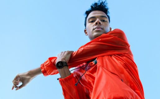 A man is stretching his left arm and is getting ready for a workout. He is wearing a black Galaxy Watch4 device on his right wrist.